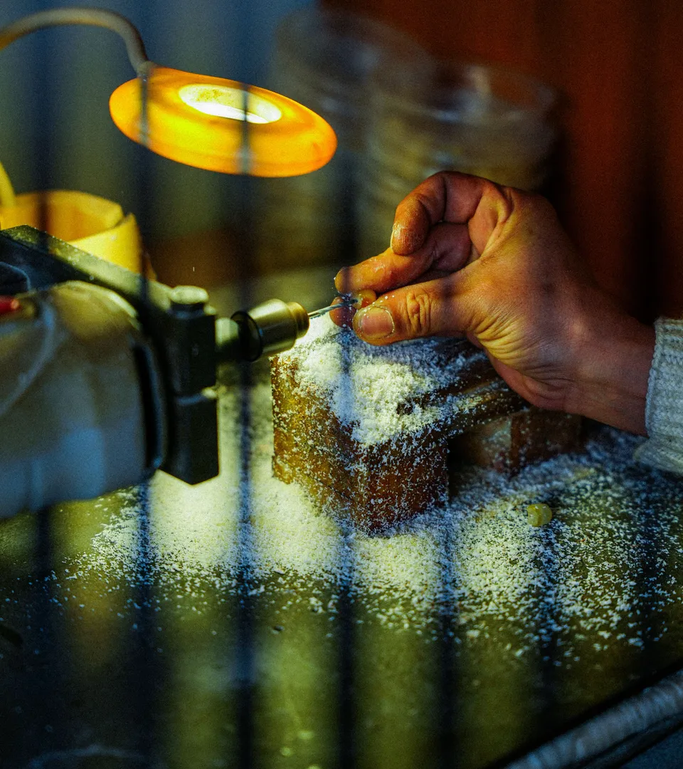 Handen van een goudsmid aan het werk in het atelier, warm verlicht met gouden tinten